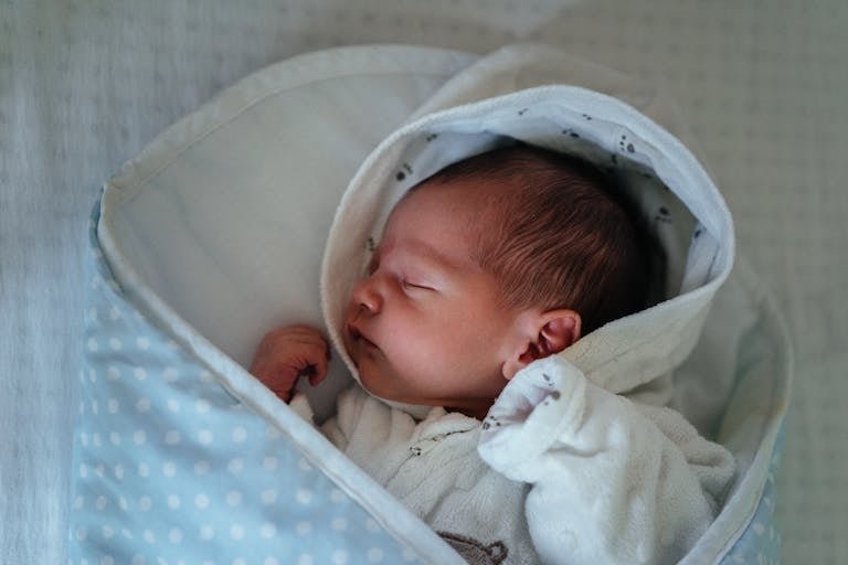 A serene newborn baby peacefully sleeping in a cozy, blue polka dot blanket indoors.